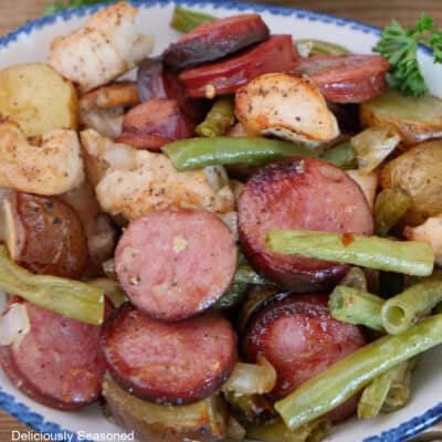 A serving of sheet pan chicken and sausage in a white bowl with blue trim.