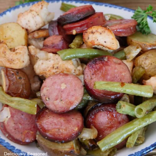 A serving of sheet pan chicken and sausage in a white bowl with blue trim.
