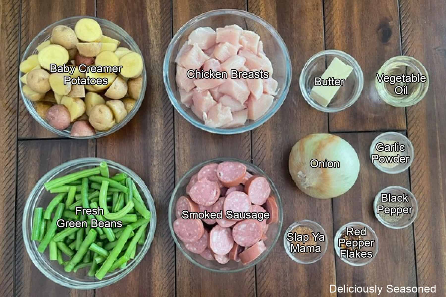 A wood surface with all the ingredients placed on it to make sheet pan chicken and sausage.