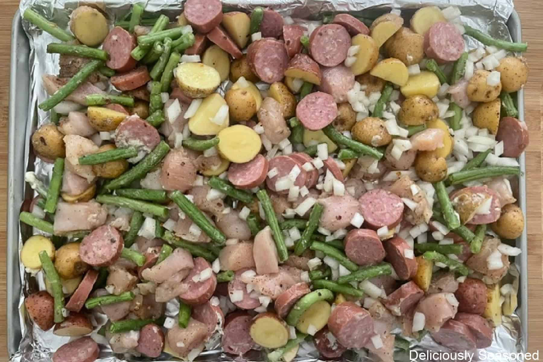 A foil lined large baking sheet with all the ingredients for sheet pan chicken and sausage spread out in an even layer before going into the oven.