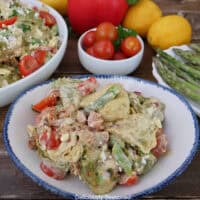 A white bowl with blue trim filled with a serving of tortellini pasta salad placed on a rustic wood surface.