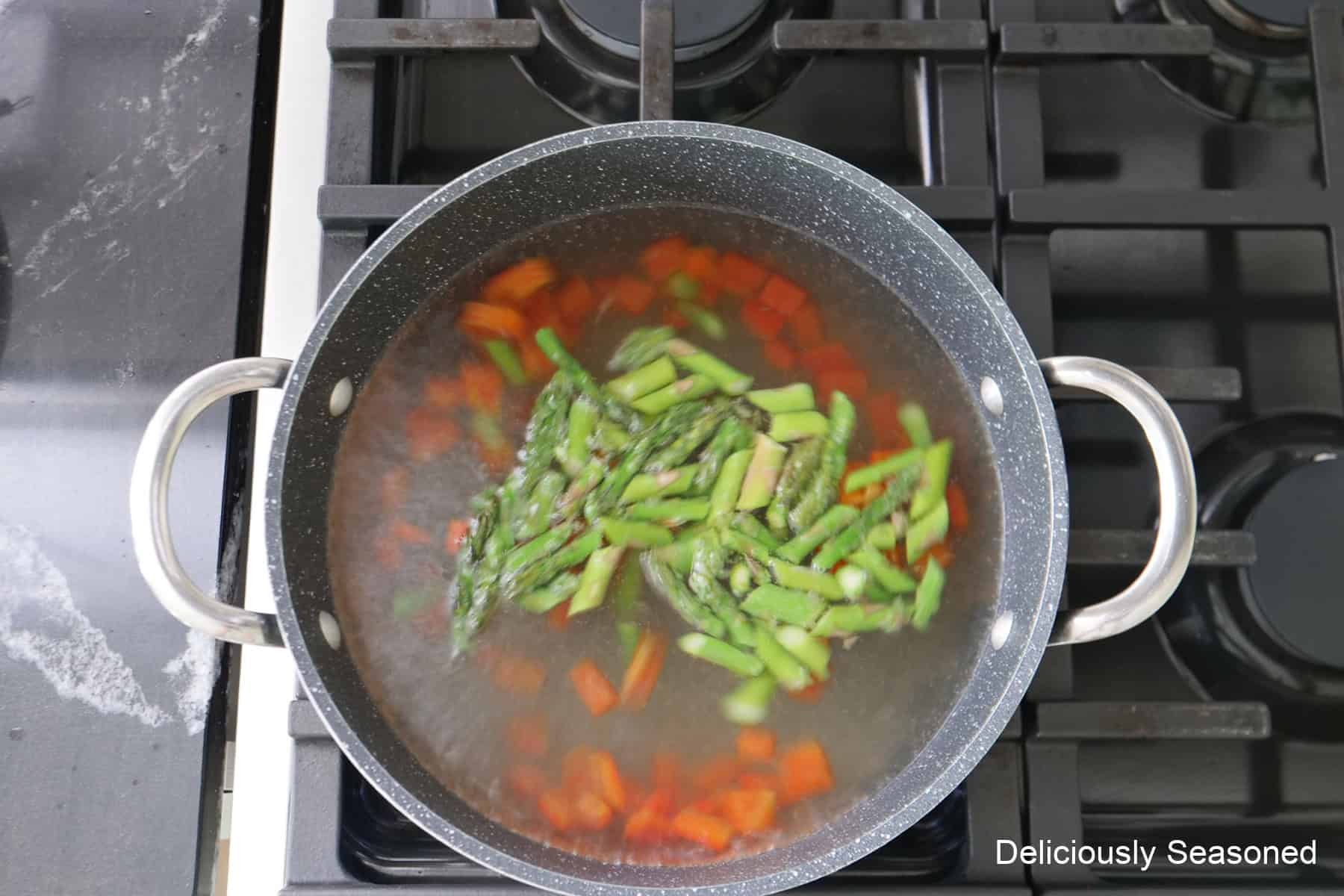 A saucepan on the stove filled with water and parboiling diced red bell peppers and asparagus.