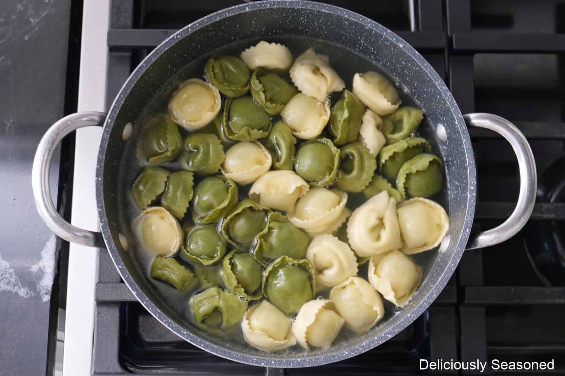 A saucepan on the stove with spinach and cheese tortellini boiling in it.