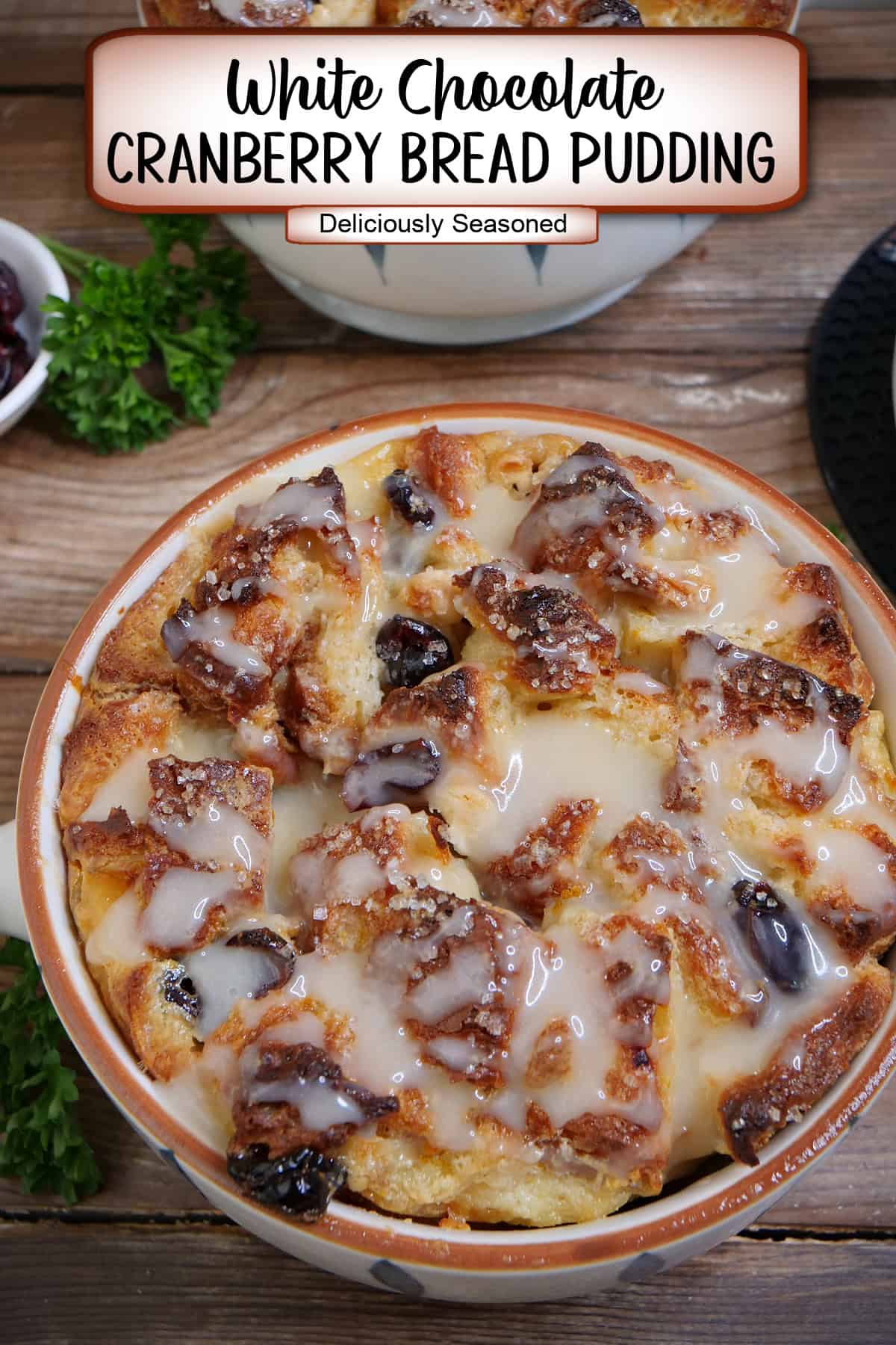 A rustic wood surface with a round baking dish with a white chocolate cranberry bread pudding in it with a title overlay at the top.