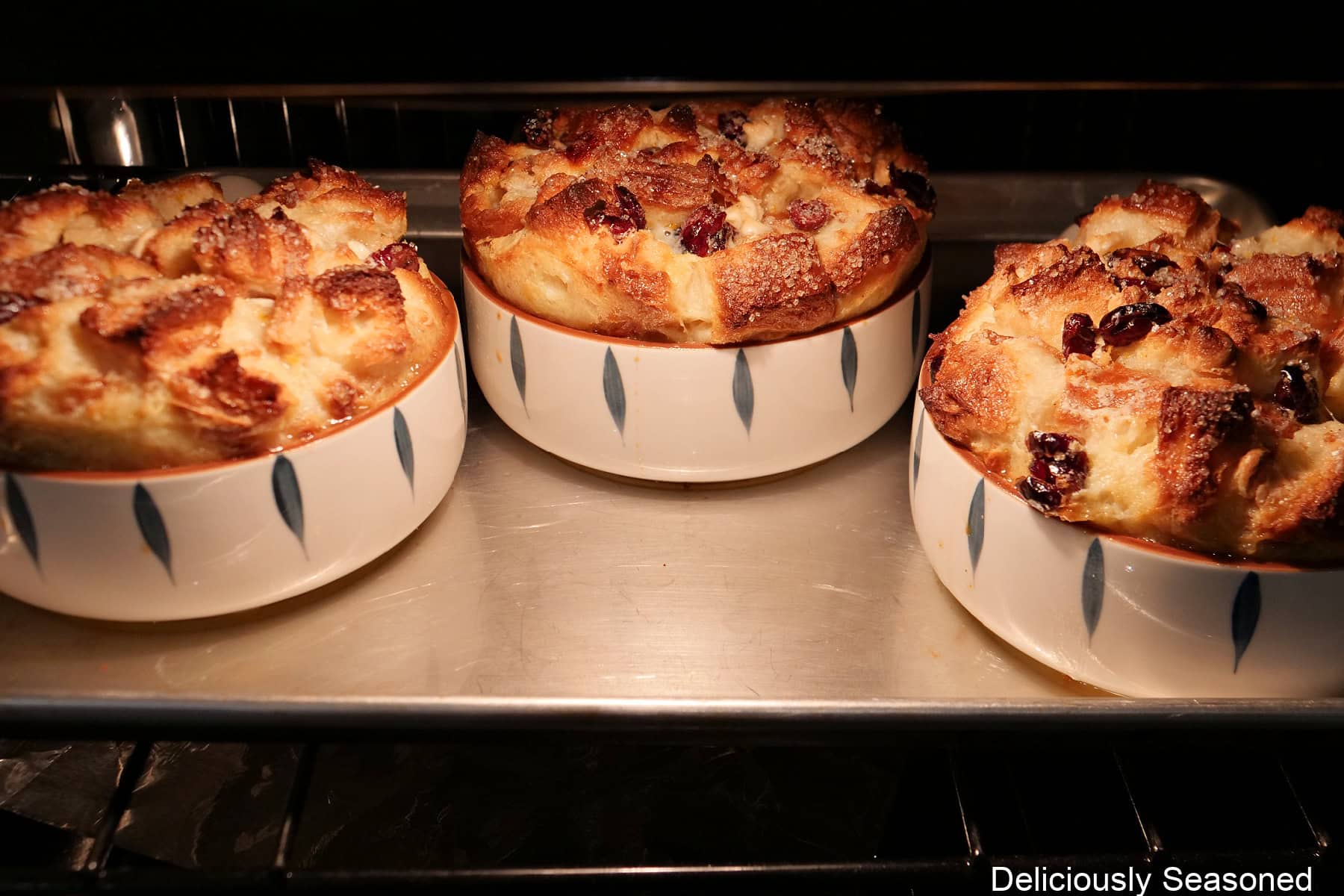 A baking sheet with three baking dishes filled with white chocolate cranberry bread pudding in the oven baking.
