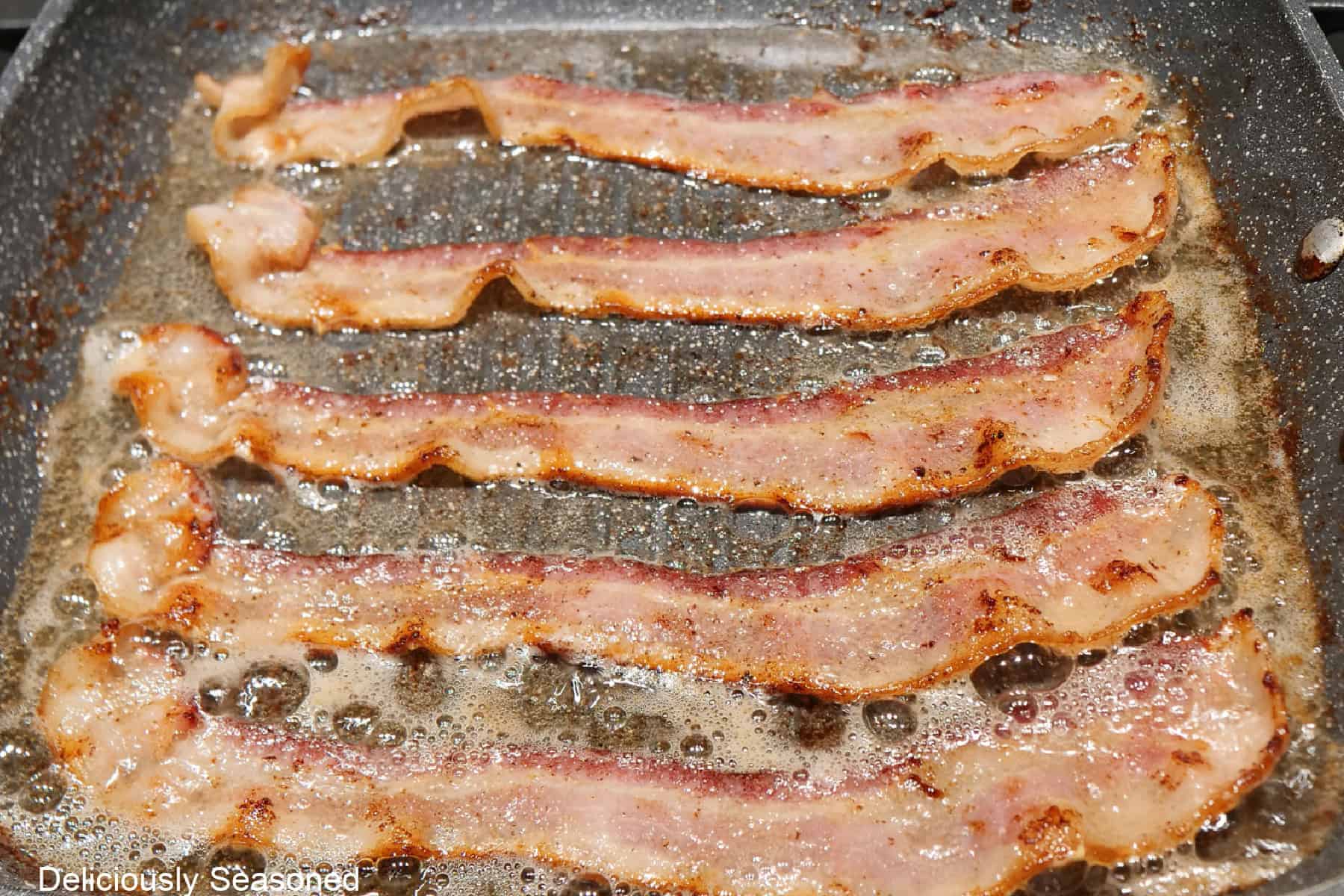 A frying pan with five strips of bacon being fried.