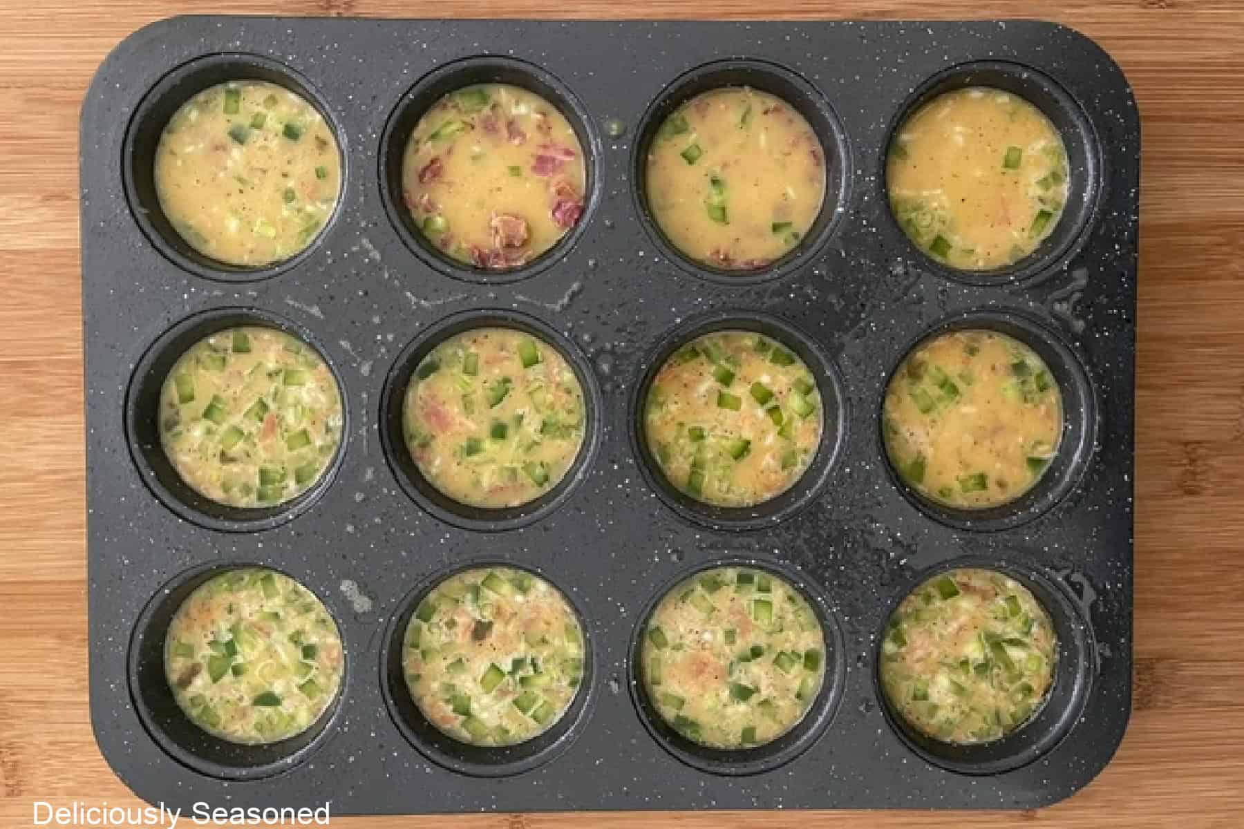 A wood surface with a 12-count baking tin filled with the egg bite mixture.