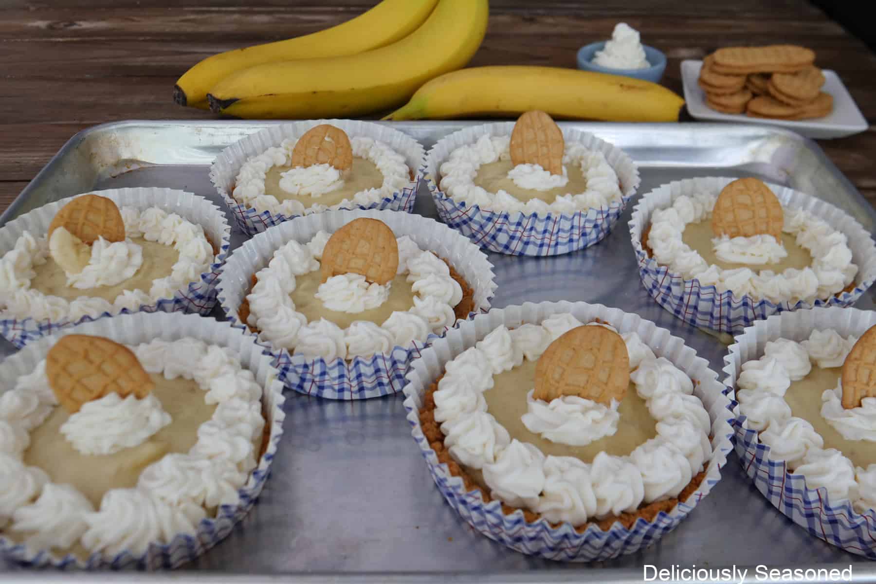 A silver baking sheet with eight banana pudding dessert cups with topped with whipped cream and a piece of Nutter Butter peanut butter cookies.