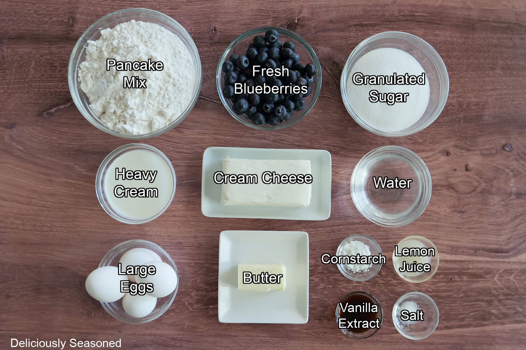 A wood surface with all the ingredients placed on it to make blueberry waffle cheesecake.