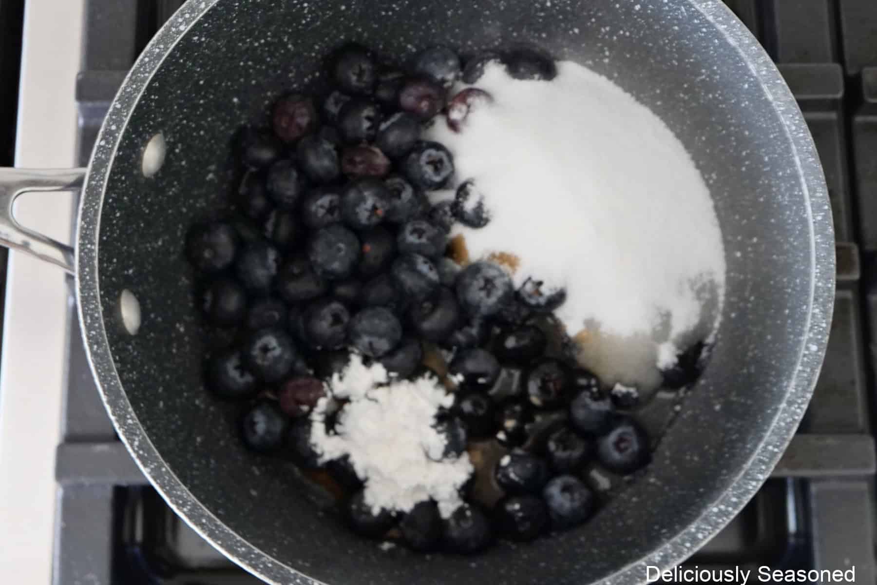 A saucepan on the stove with the blueberry filling ingredients in it.