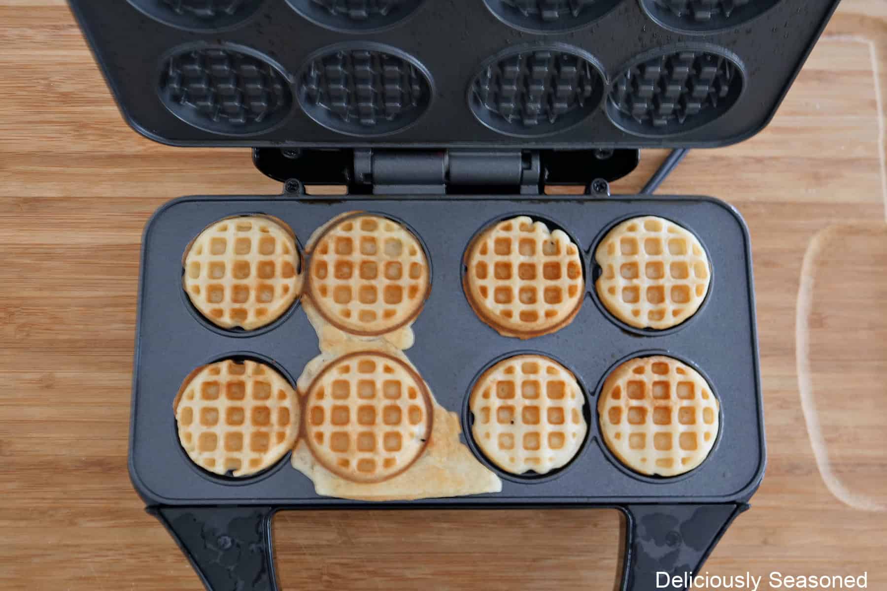 A mini waffle maker with eight mini cooked waffles in it.