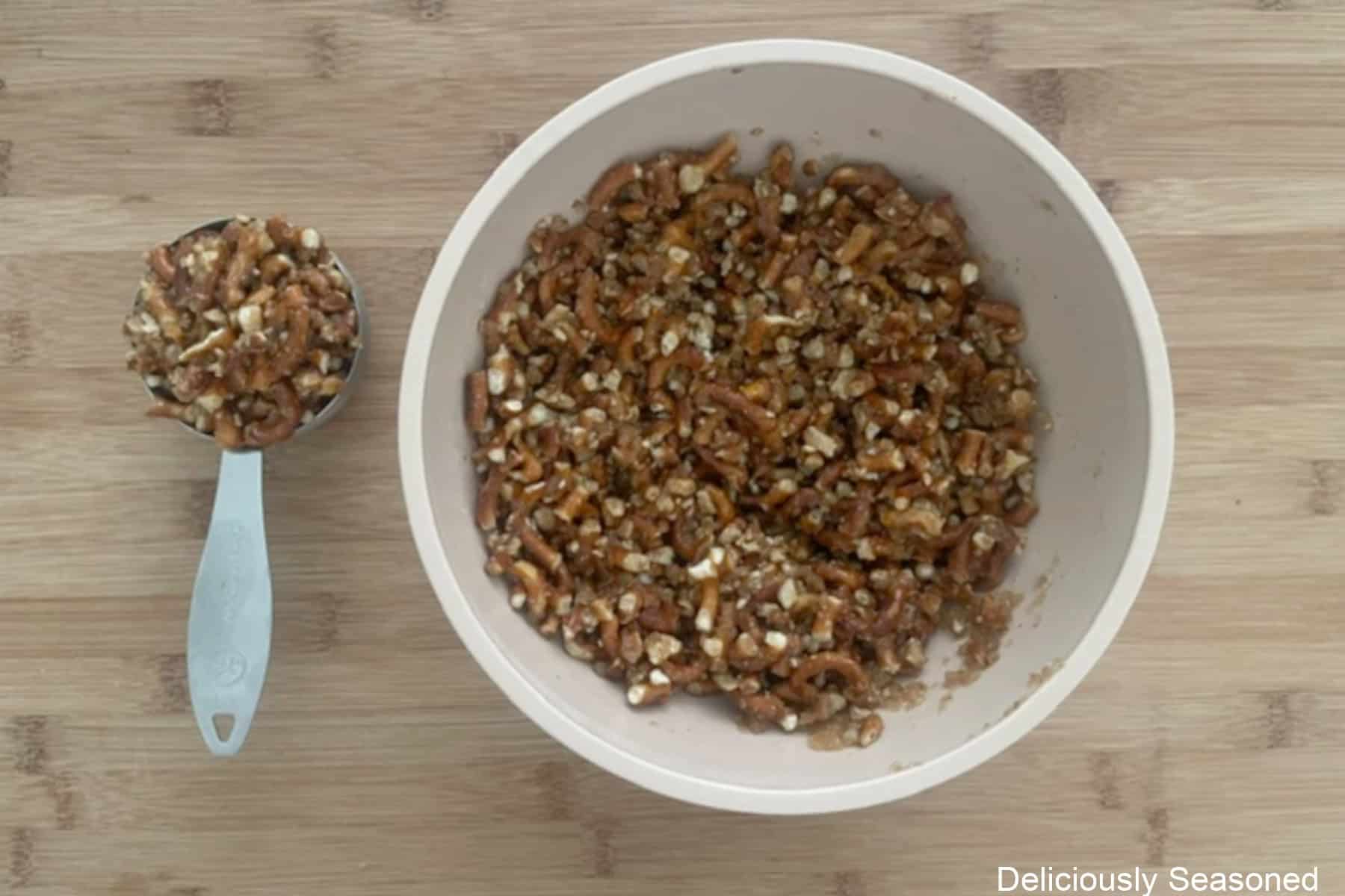 A wood surface with a bowl and measuring cup filled with pretzel crust mixture.