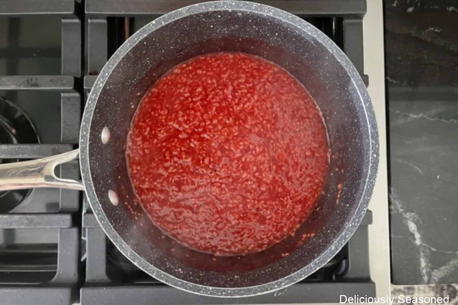 a saucepan on a stovetop cooking a homemade raspberry filling.