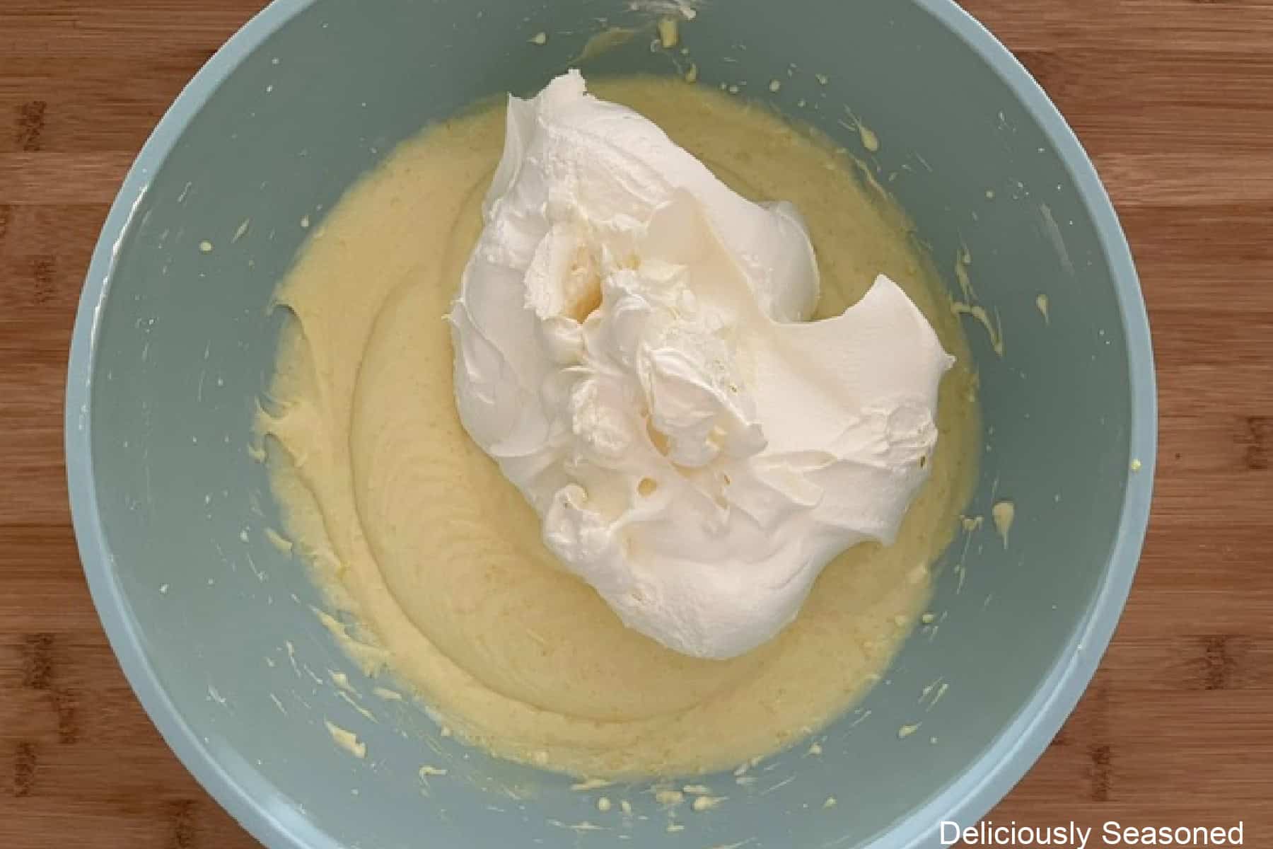 A mixing bowl placed on a wood surface with a lemon cream cheese mixture and cool whip in it.
