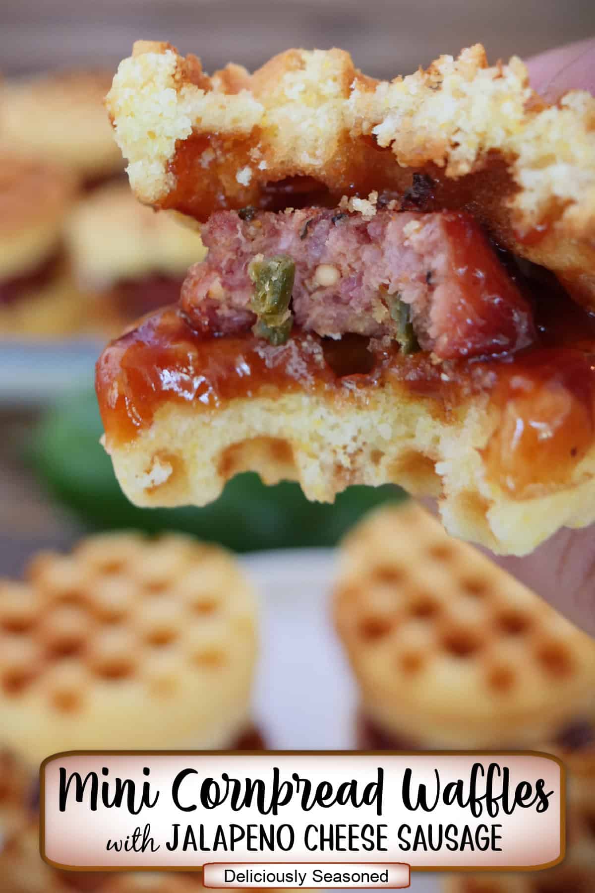 A mini cornbread waffle with jalapeno cheese sausage, held above other mini waffles, with a bite taken out of it.