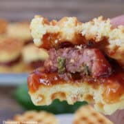 A mini cornbread waffle with jalapeno cheese sausage inside with a bite taken out of it.