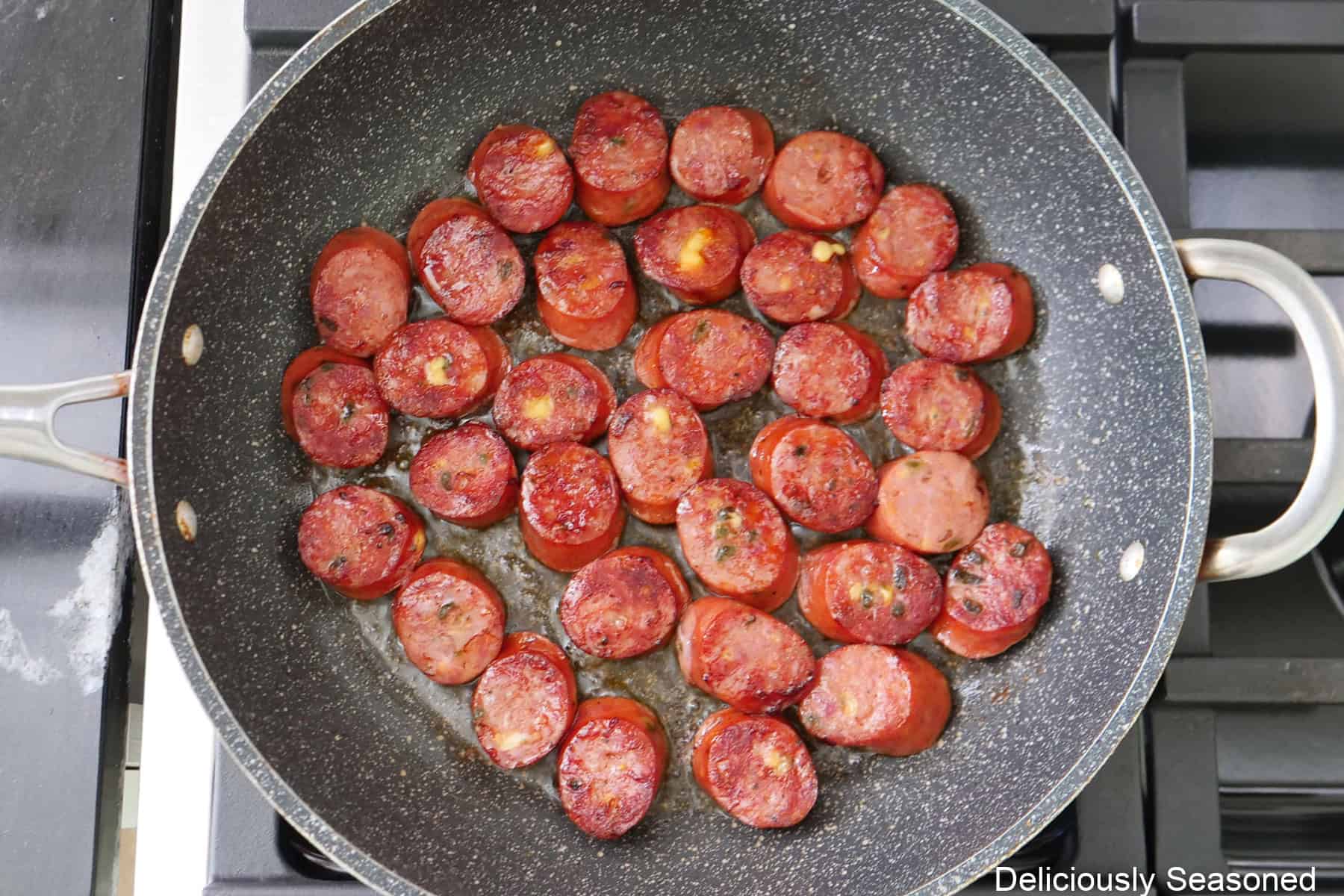 A frying pan on the stove with sliced jalapeno cheese sausage in it cooking.