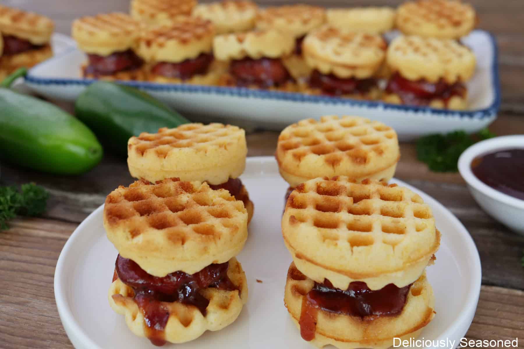 A wood surface with two white plates filled with mini cornbread waffles with jalapeno cheese sausage in the middle,