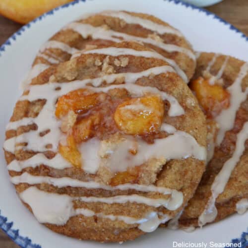 A round white plate with blue trim with three peach cobbler brown butter snickerdoodles on it with peaches in the background.