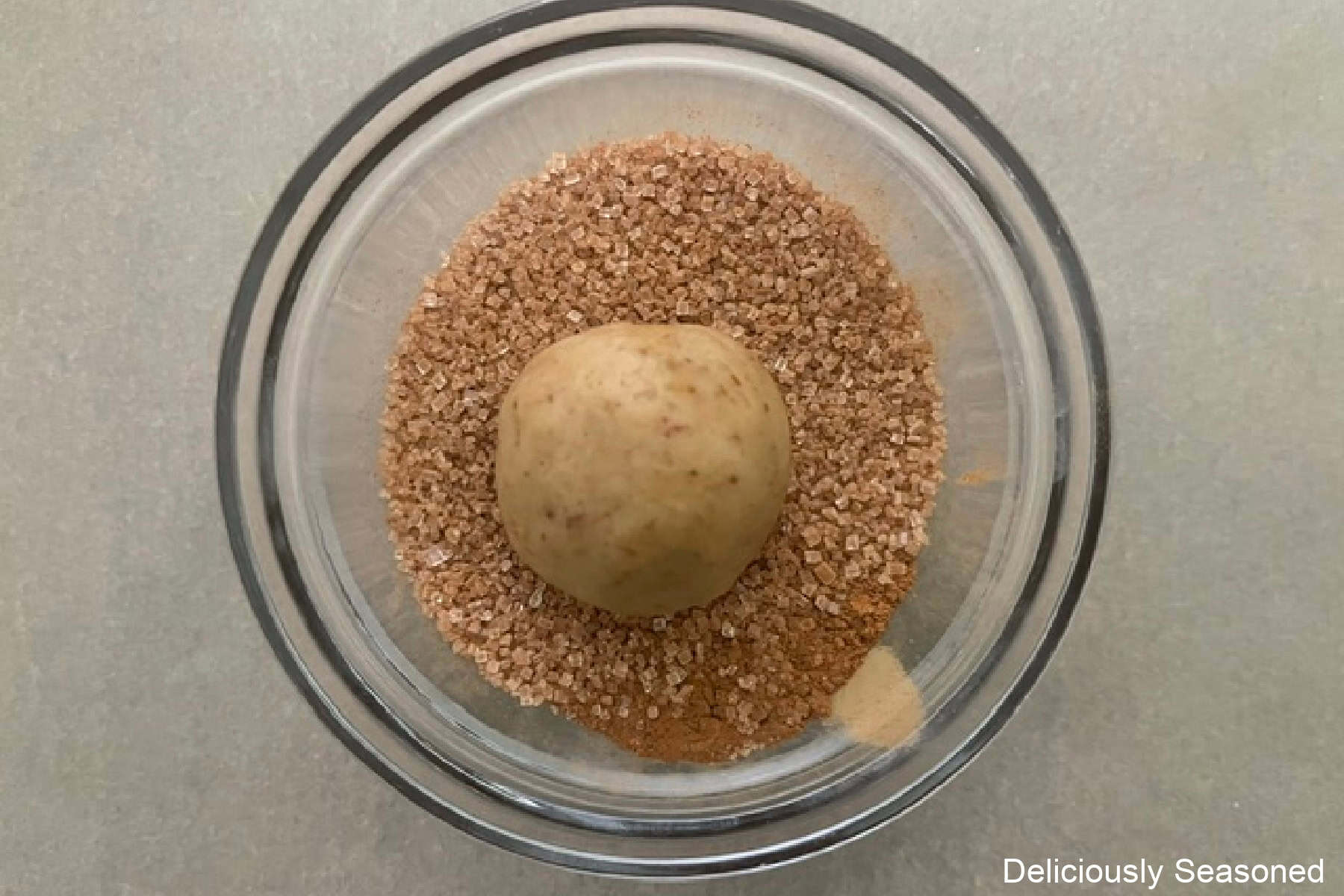 A small glass bowl with cinnamon sugar mixture in it with a snickerdoodle cookie dough ball in it.