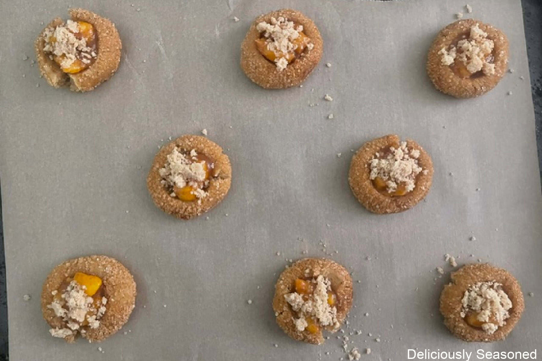 A parchment lined baking sheet with eight peach cobbler brown butter snickerdoodle cookies placed on it before being baked.