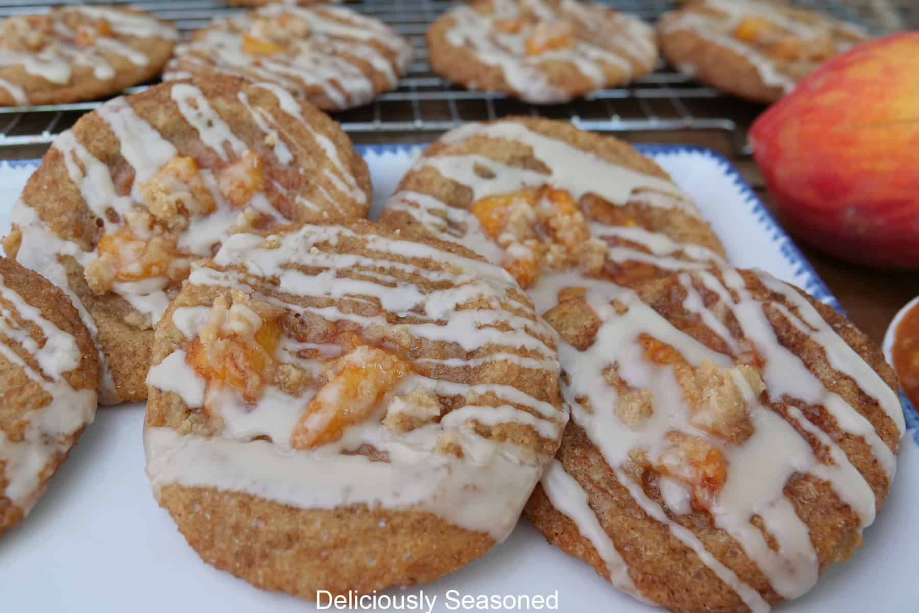 A white plate with five peach cobbler brown butte snickerdoodle cookies on it with more cookies on a wire rack in the background.