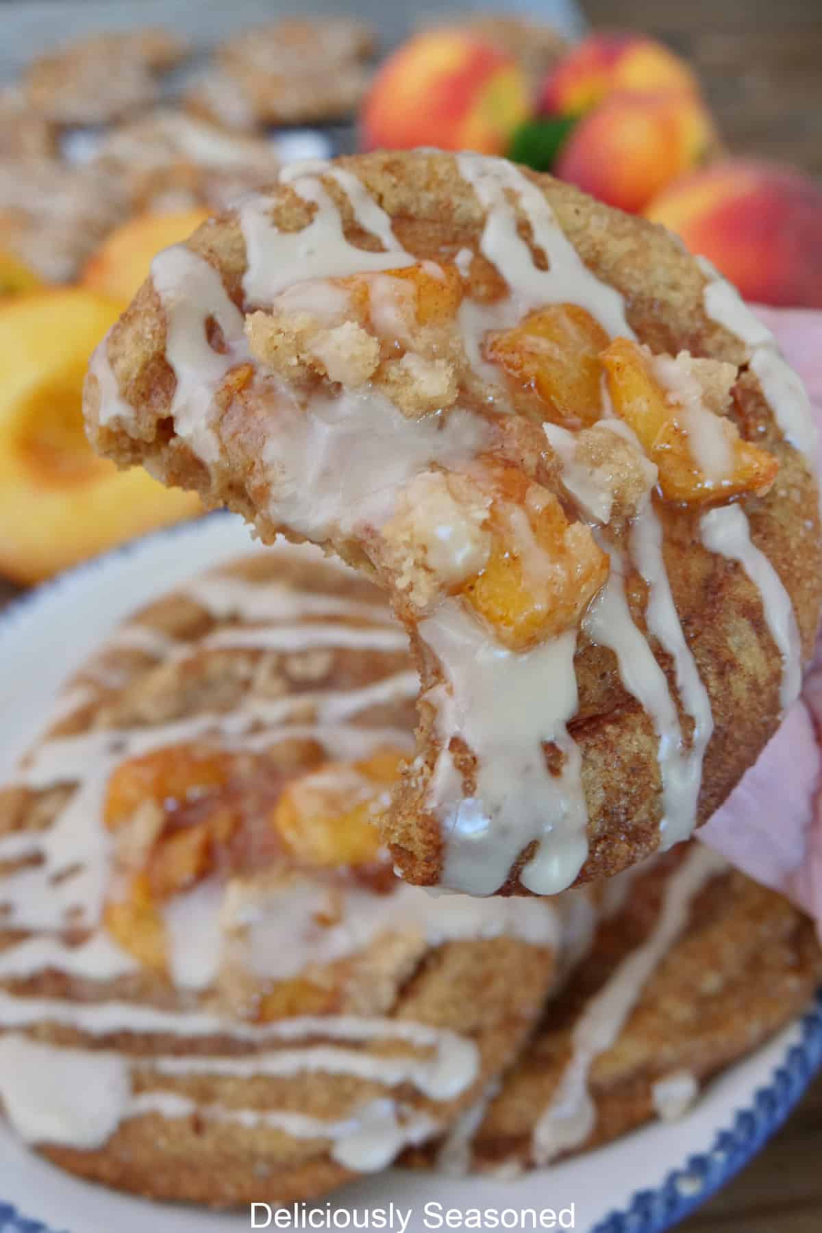 A few peach cobbler brown butter snickerdoodles on a white plate with blue trim and one cookie held up above the plate with a bite taken out of it.