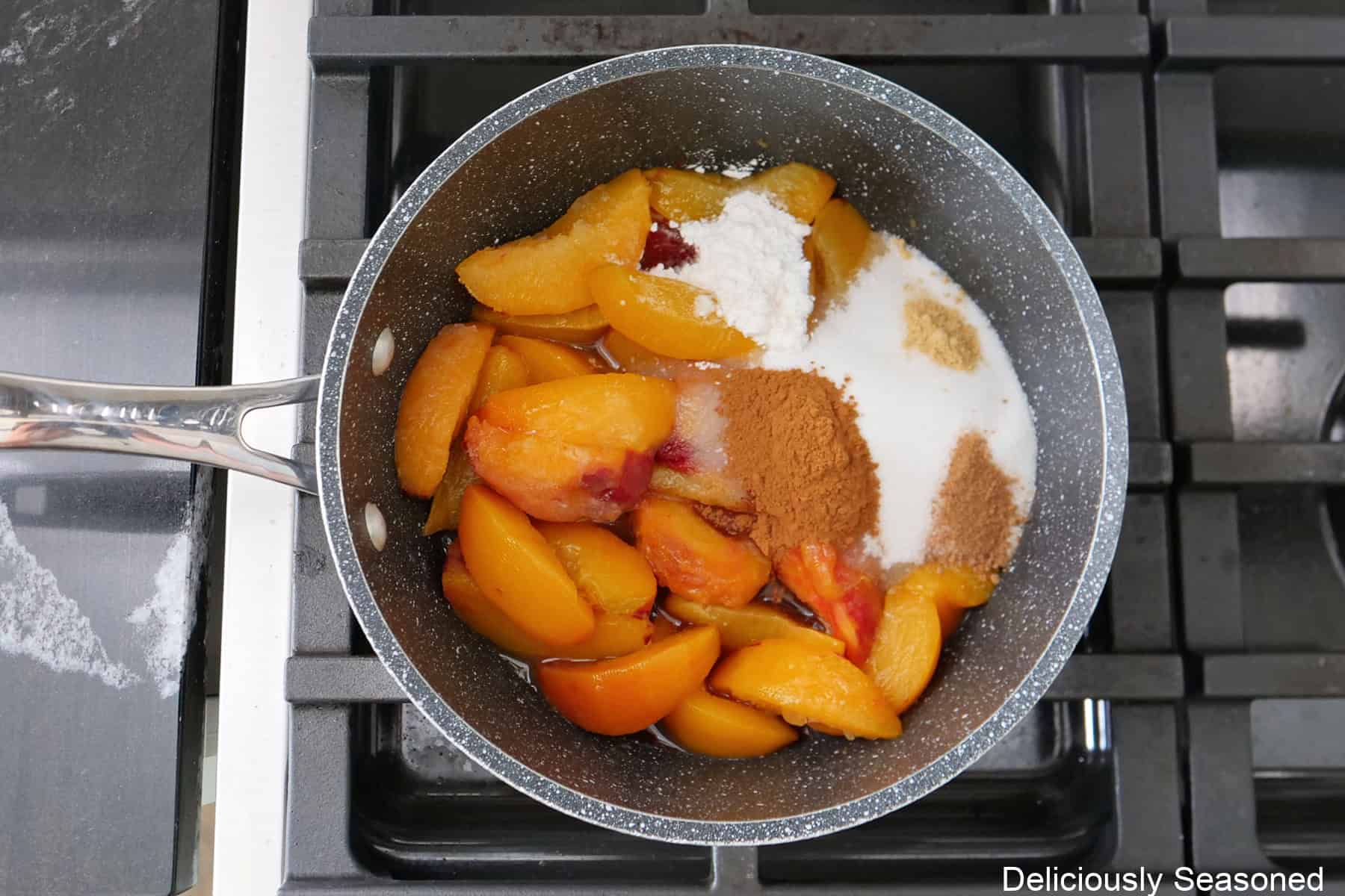 A saucepan with sliced peaches and the remaining filling ingredients in the pan before being stirred together.