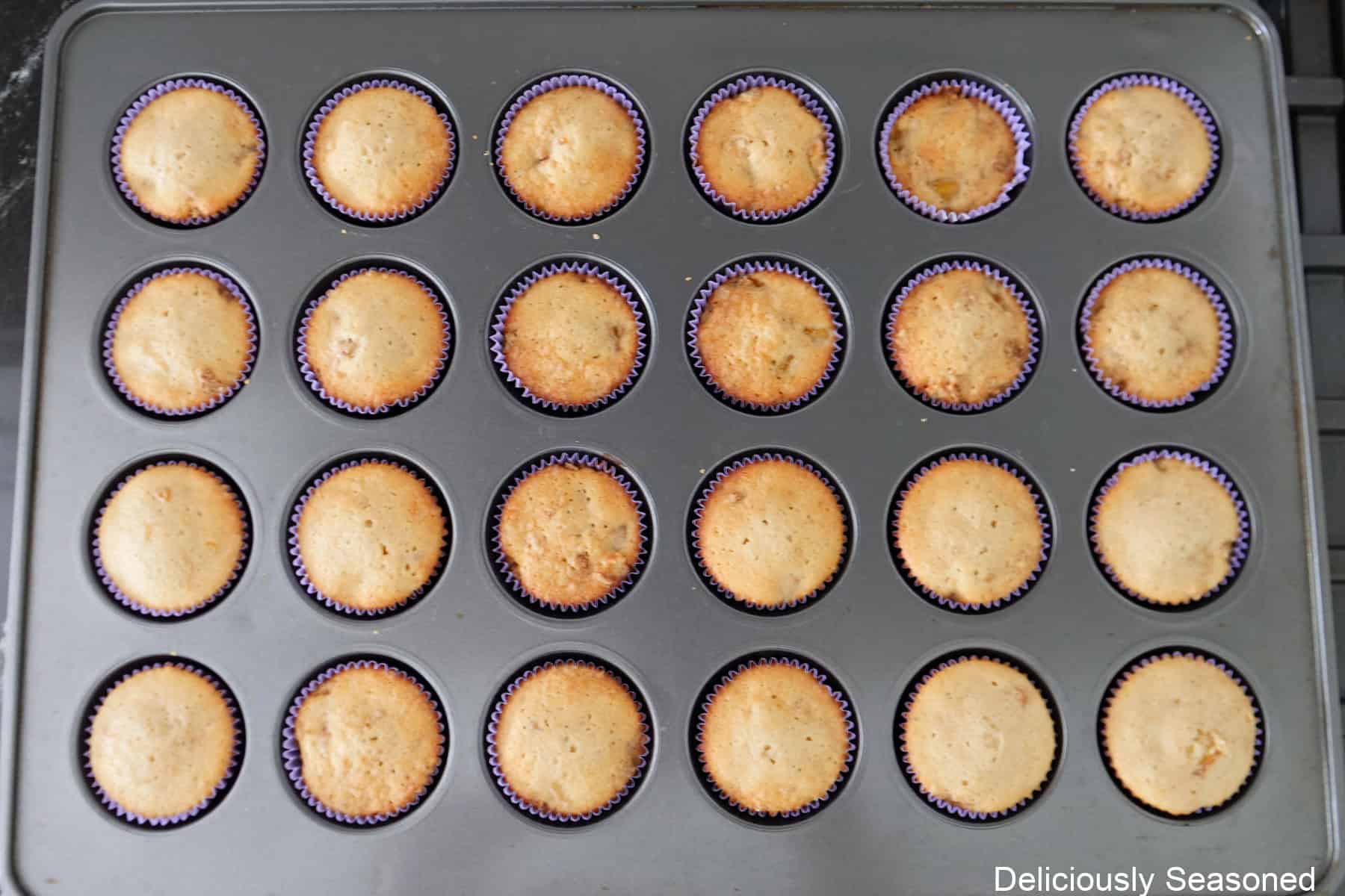 A 24-count muffin tin filled with baked peach cobbler cupcakes.