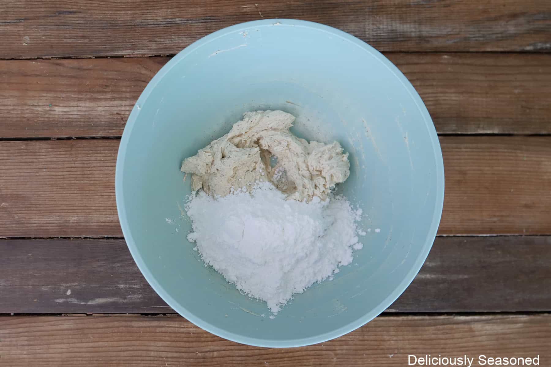 A wood surface with a light blue bowl with the brown butter frosting ingredients in it.