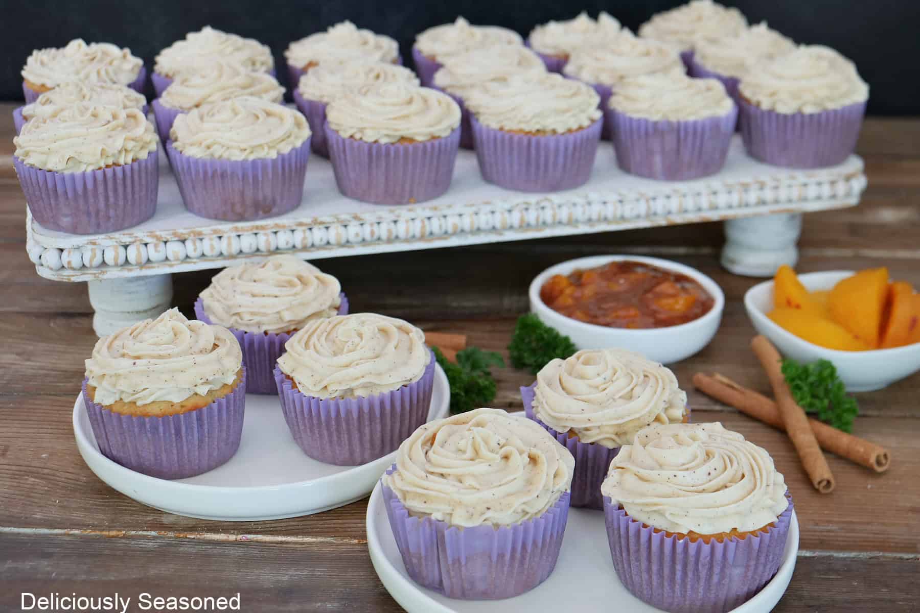 A rustic wood surface with peach cobbler cupcakes placed on white plates and a white tray.