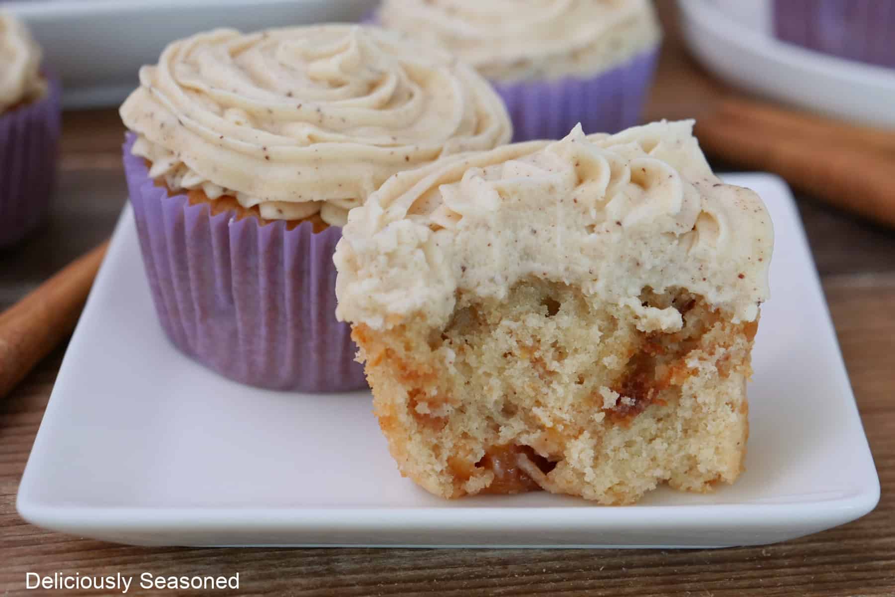 A white square plate with three cupcakes on it with a bite taken out of the cupcake in front.