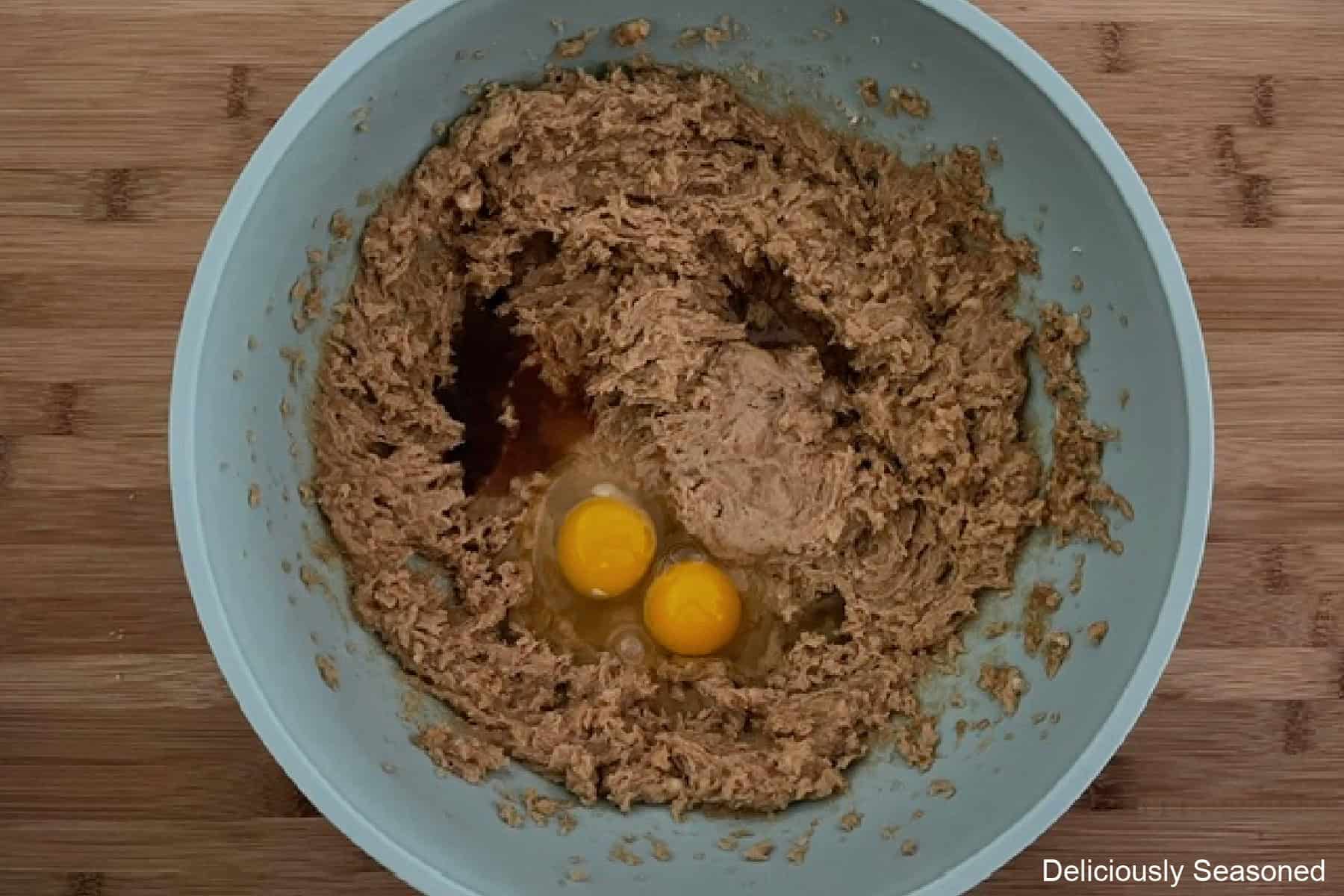 A wood surface with a blue bowl filled with the wet cookie ingredients in it before being mixed together.