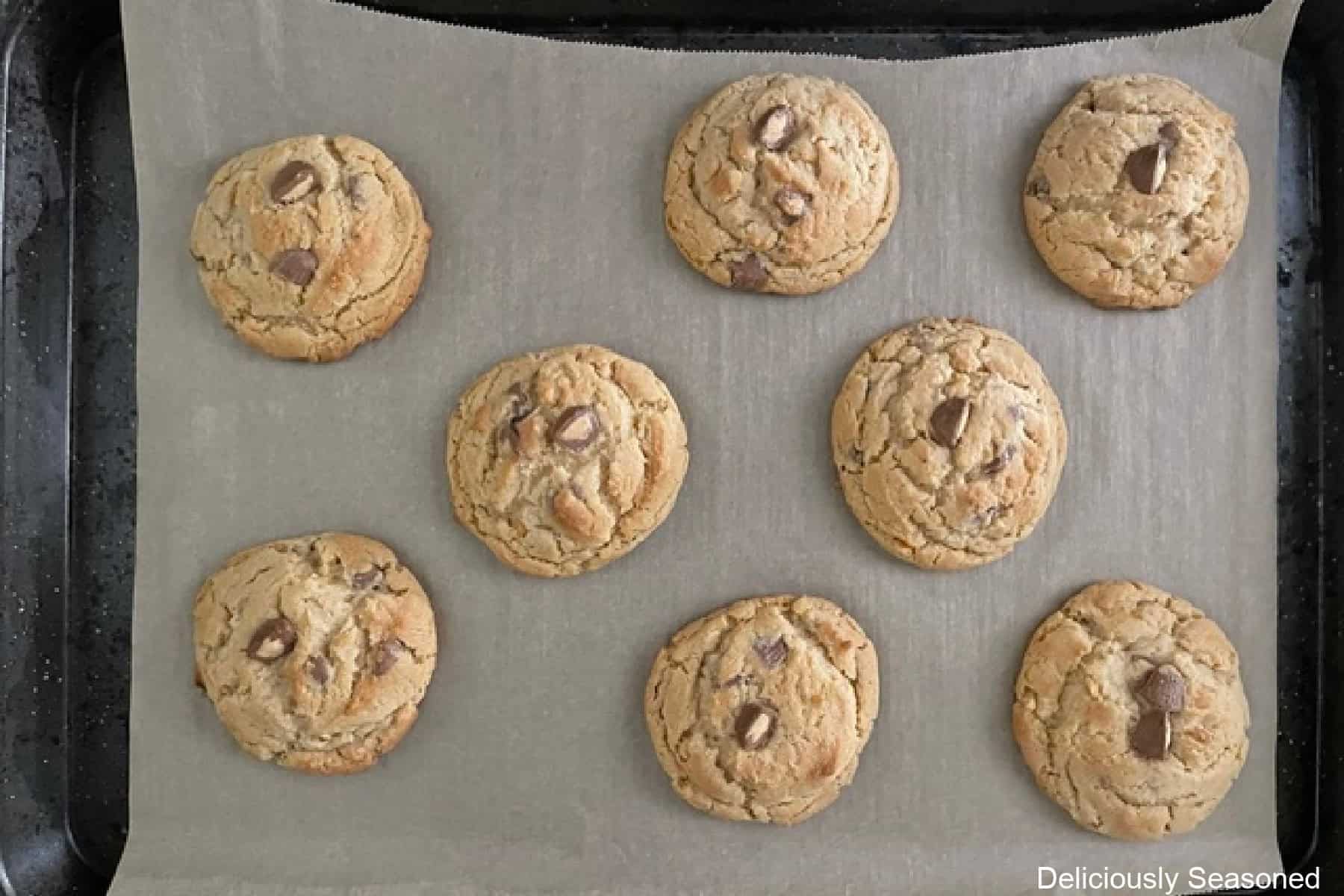 A cookie sheet with parchment paper on it with eight baked peanut butter cup cookies on it.