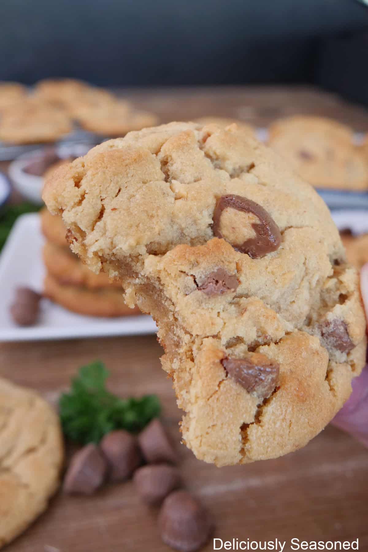 A peanut butter cup cookie with a bite taken out of it held up above more cookies on a wood surface.