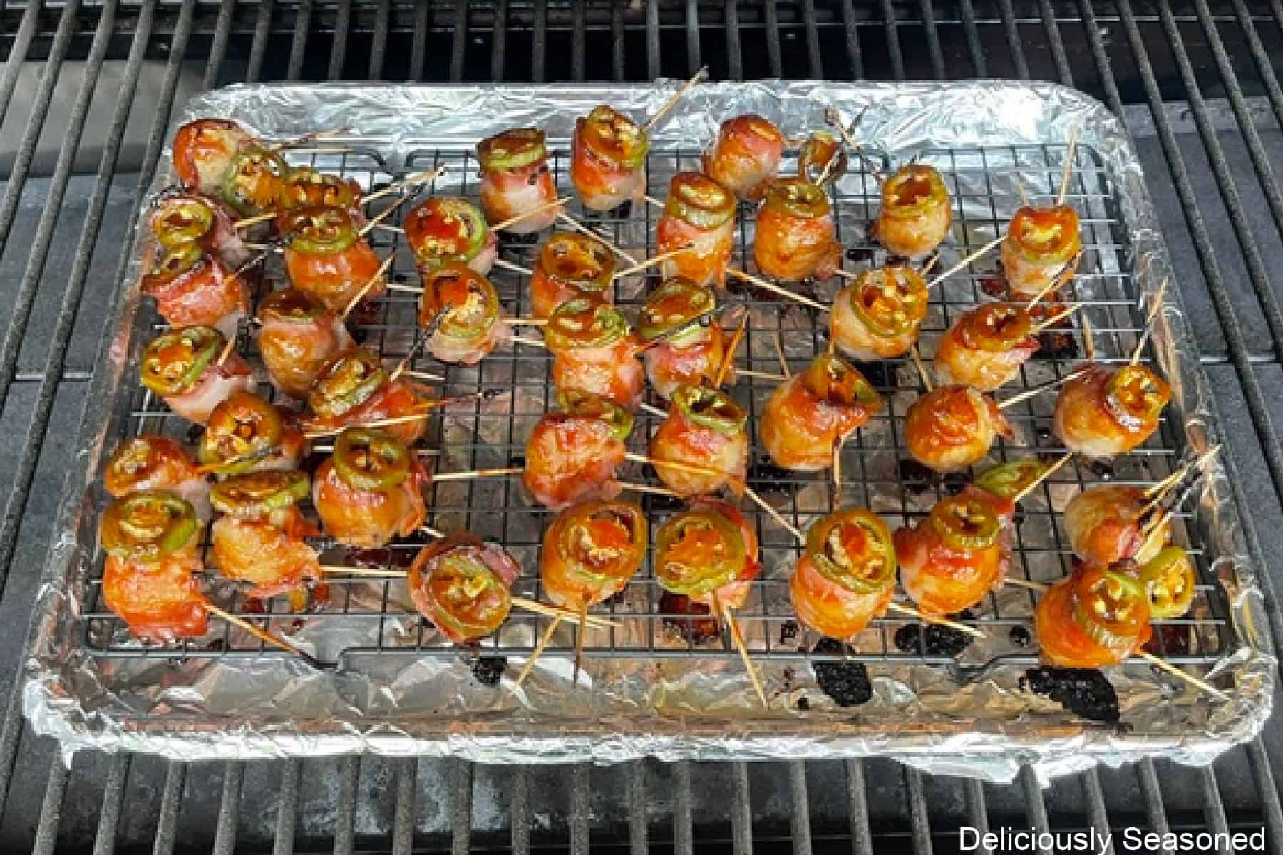 A foil lined baking sheet on the smoker grill grates filled with bacon wrapped meatballs.