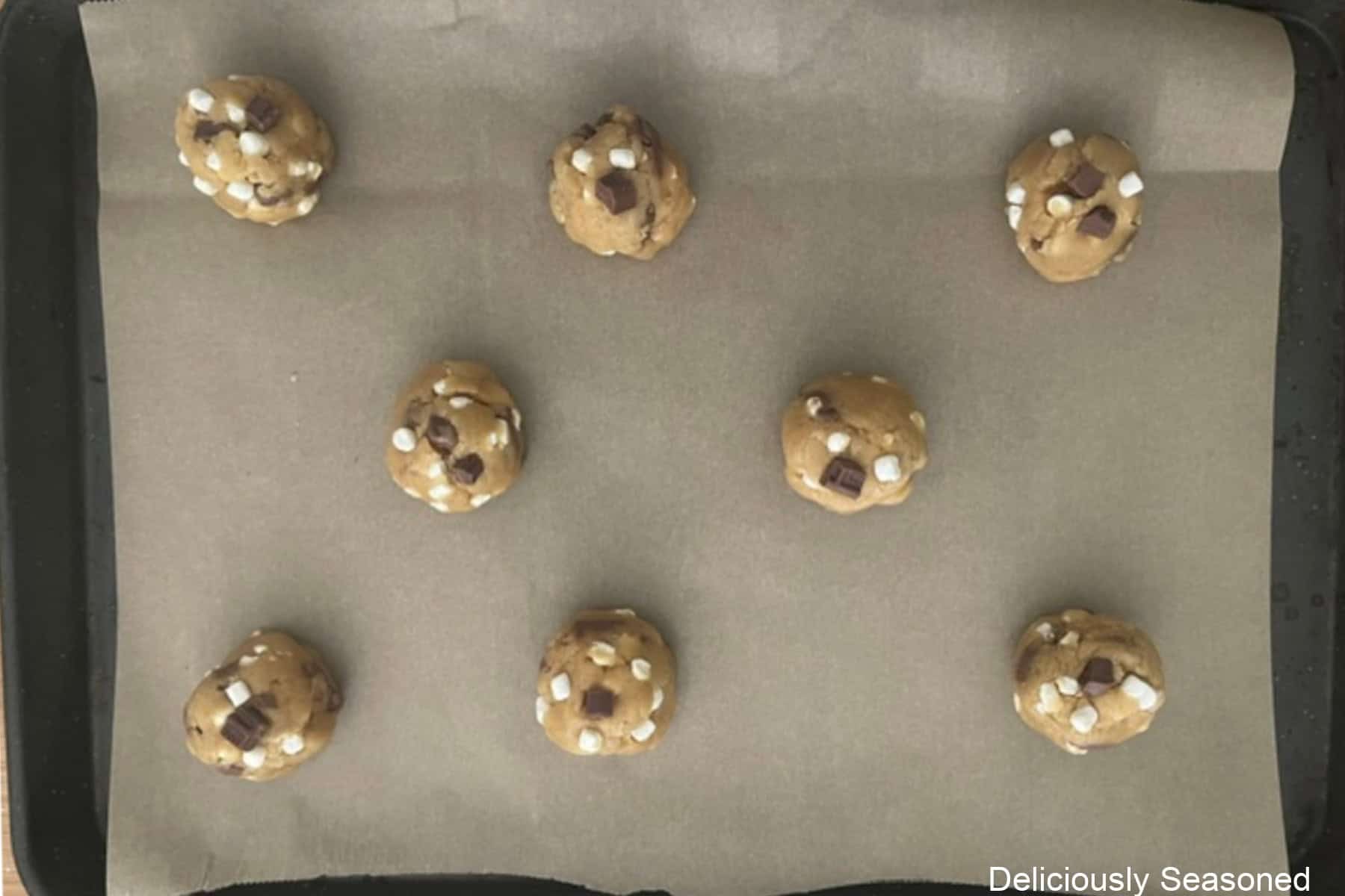 A parchment lined baking sheet with eight cookie dough balls on it.