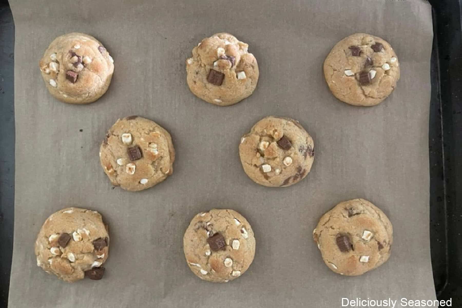 A baking sheet lined with parchment paper with eight baked s'mores cookies on it.