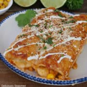 A blue trimmed white plate with two chicken street corn enchiladas on it.