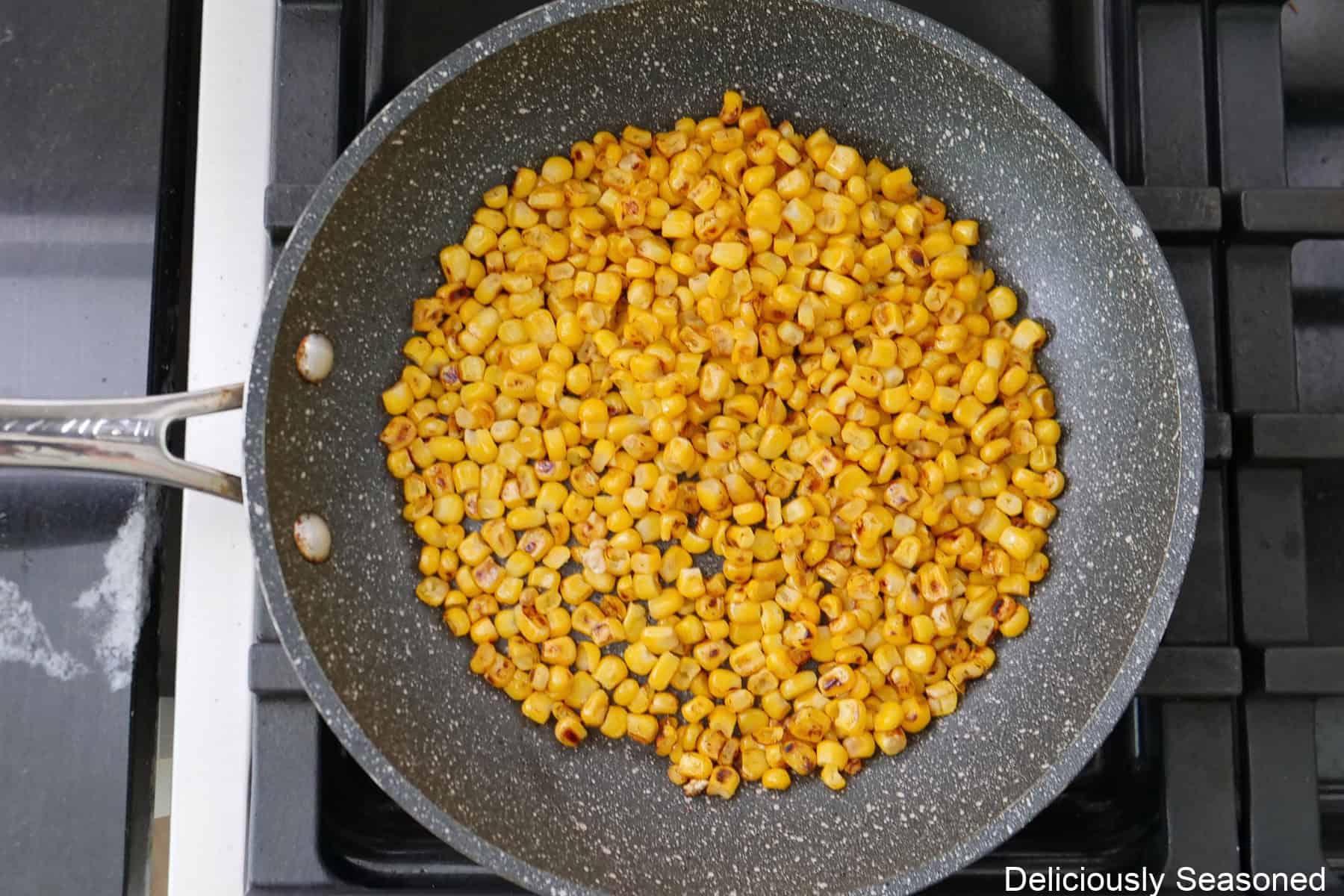 A frying pan on the stovetop with corn kernels in it being roasted.