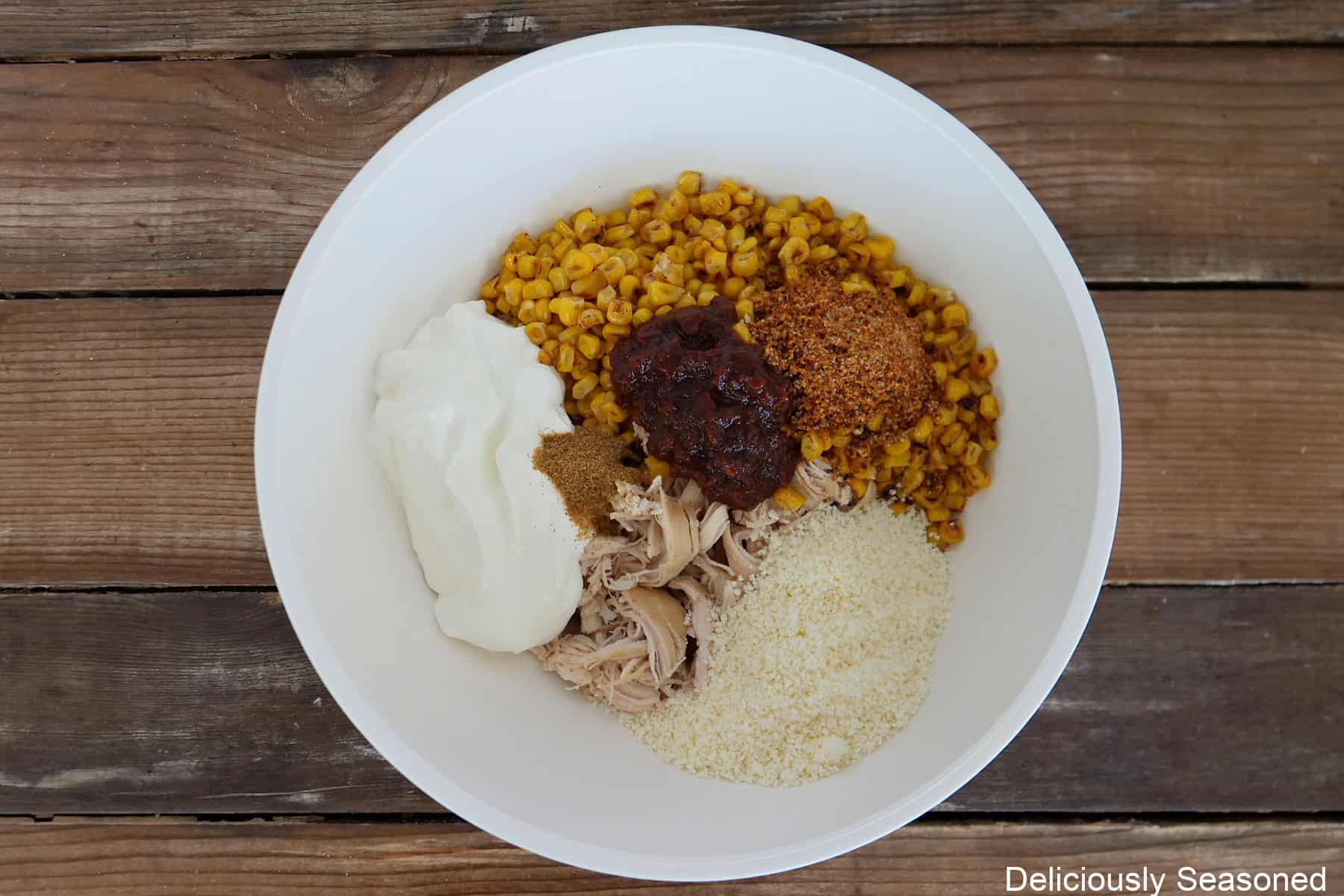 A wood surface with a white bowl filled with all the enchilada ingredients in it before being mixed together.