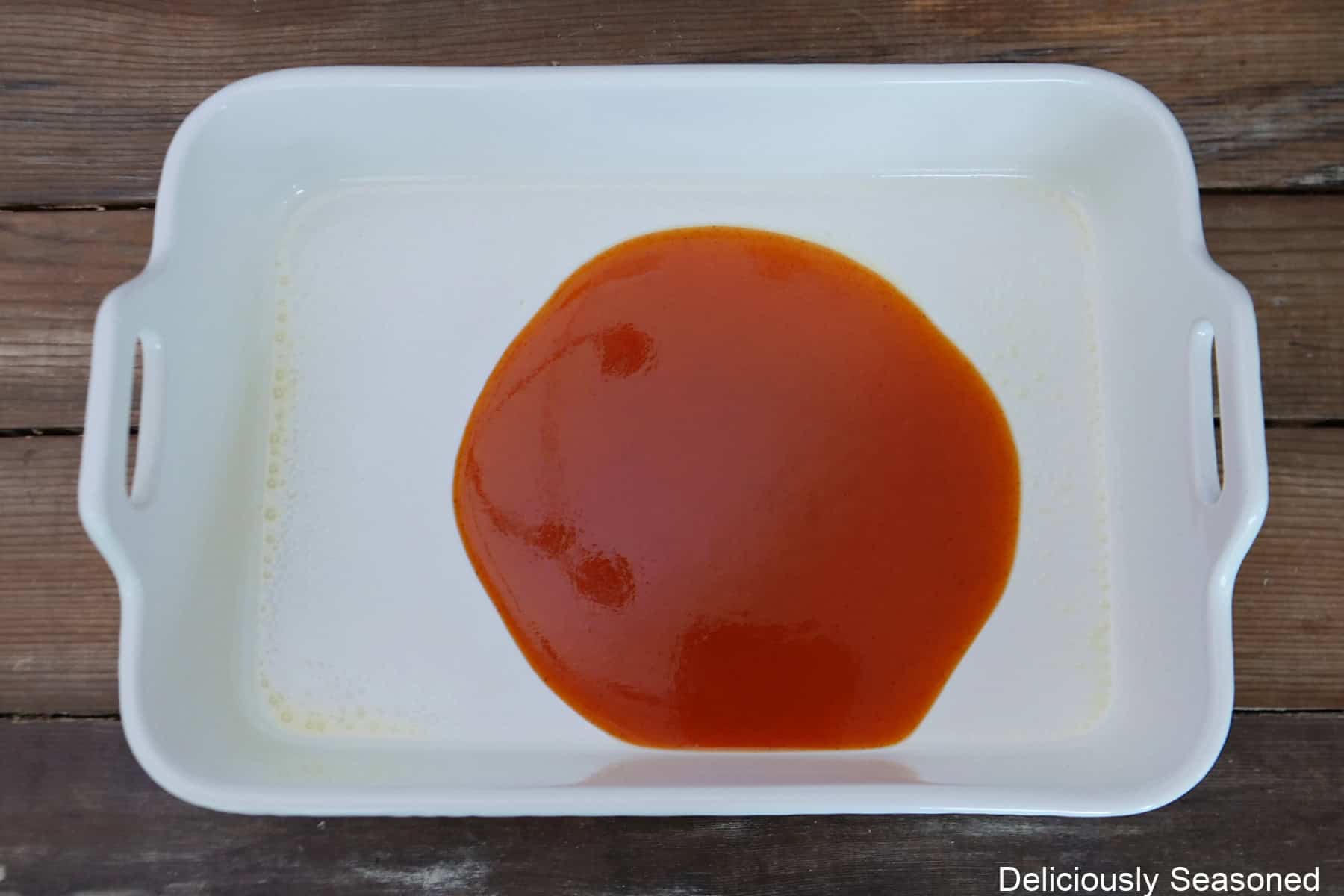 A white 13x9 inch baking dish with a small amount of red enchilada sauce in it.