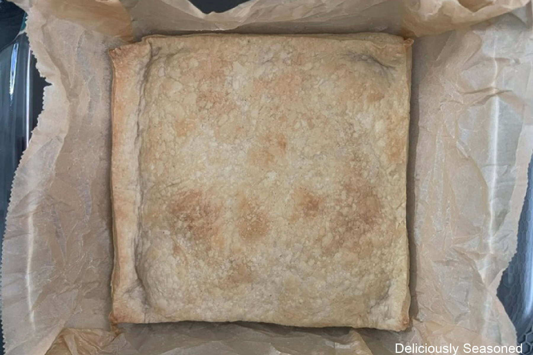 A glass baking dish lined with parchment paper with a baked bottom crust in it.