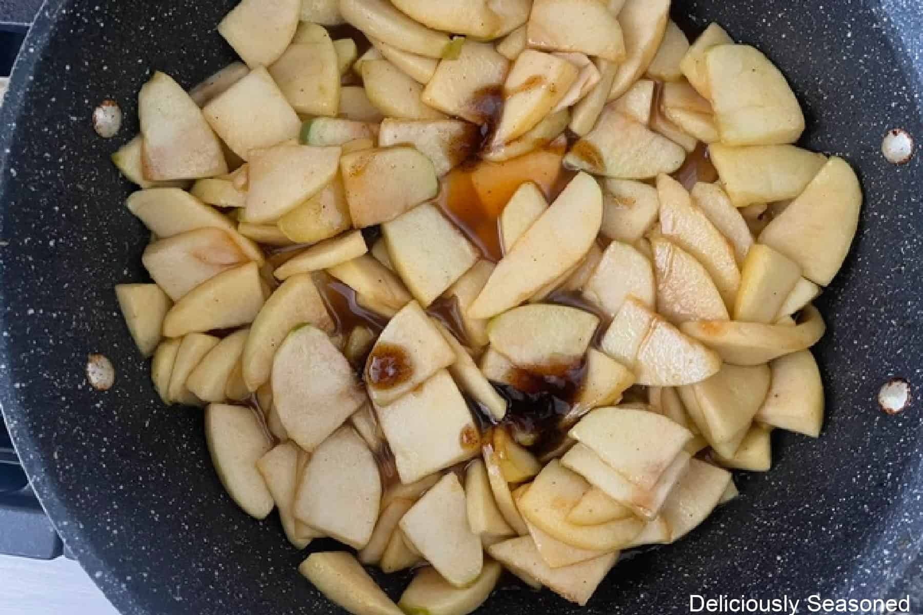 A saucepan on the stove with sliced apple pieces cooking and vanilla bean paste added.