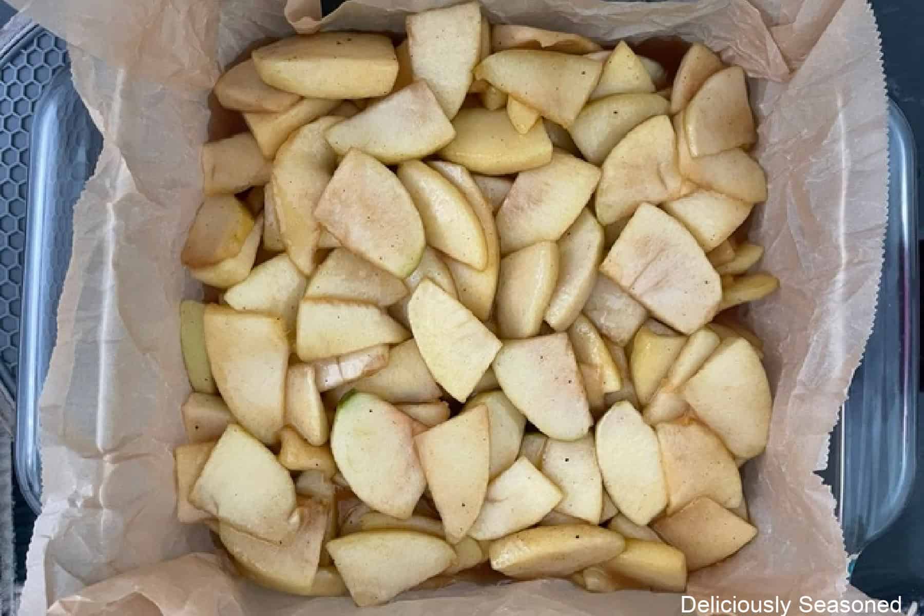 A parchment lined baking dish with apple pie filling placed over the baked bottom crust.