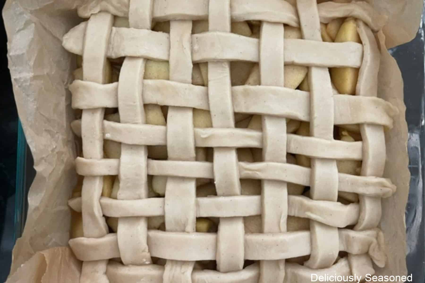 A glass baking dish with a lattice pie dough top put on top of the apple pie filling.