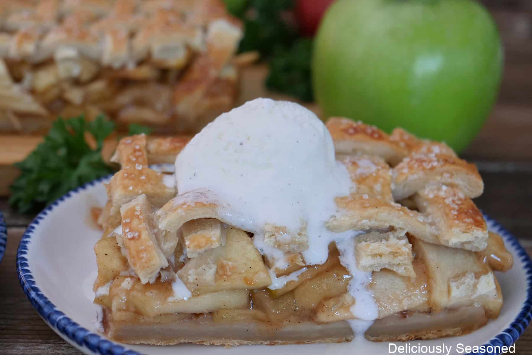 A white plate with blue trim with a serving on apple pie bars with a scoop of vanilla ice cream on top.