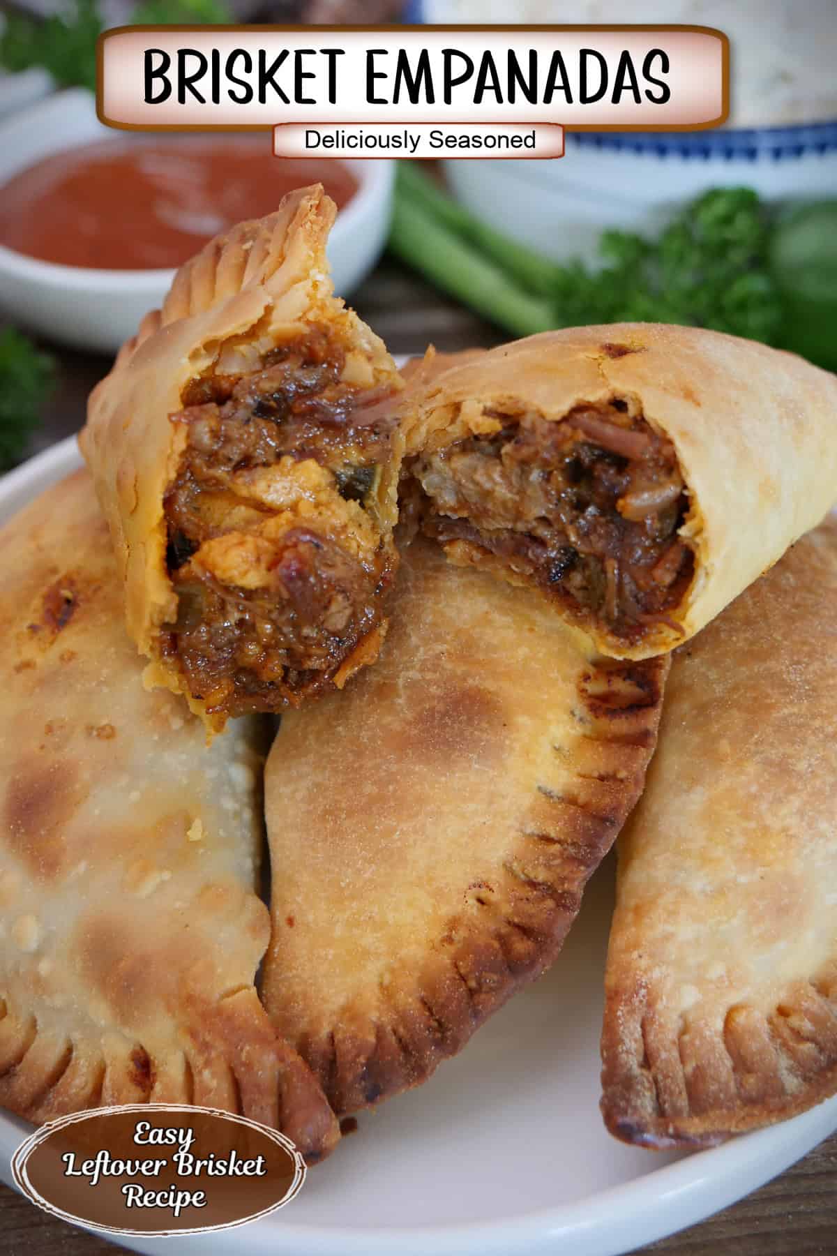 A white plate with blue trim with a small stack of beef brisket empanadas on it with the two on top showing the flaky crust and inside ingredients, and a title overlay at the top.