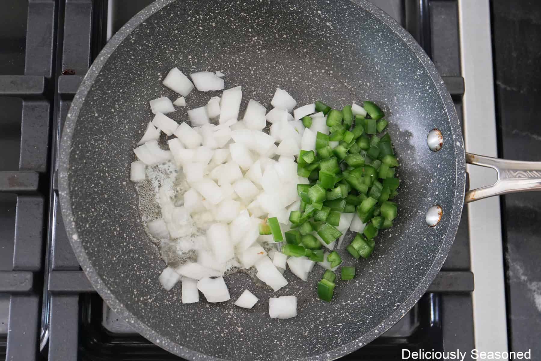 A frying pan on the stove with diced onions, jalapenos, and butter.