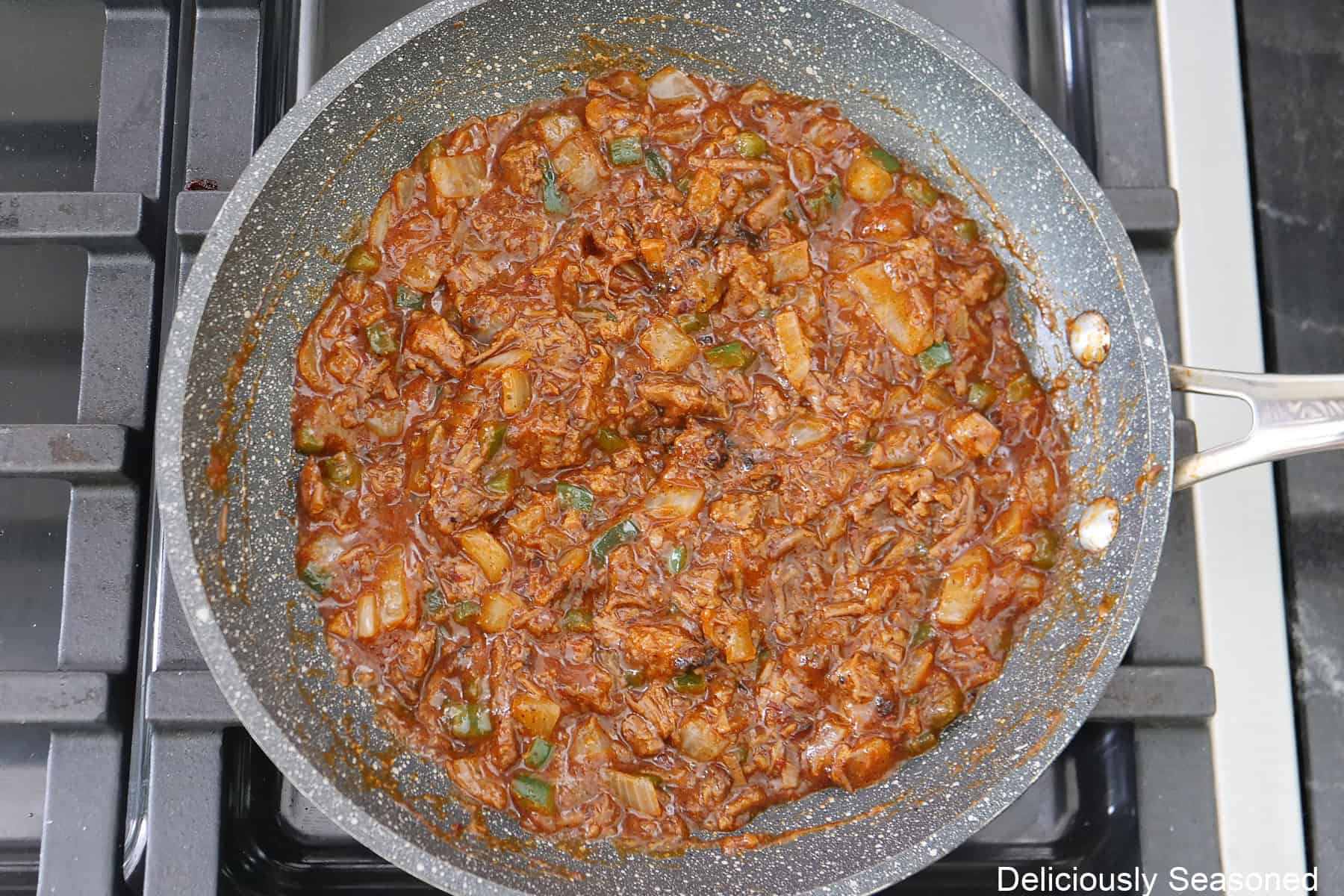 A frying pan on the stove with the beef brisket mixture all mixed together in the pan.